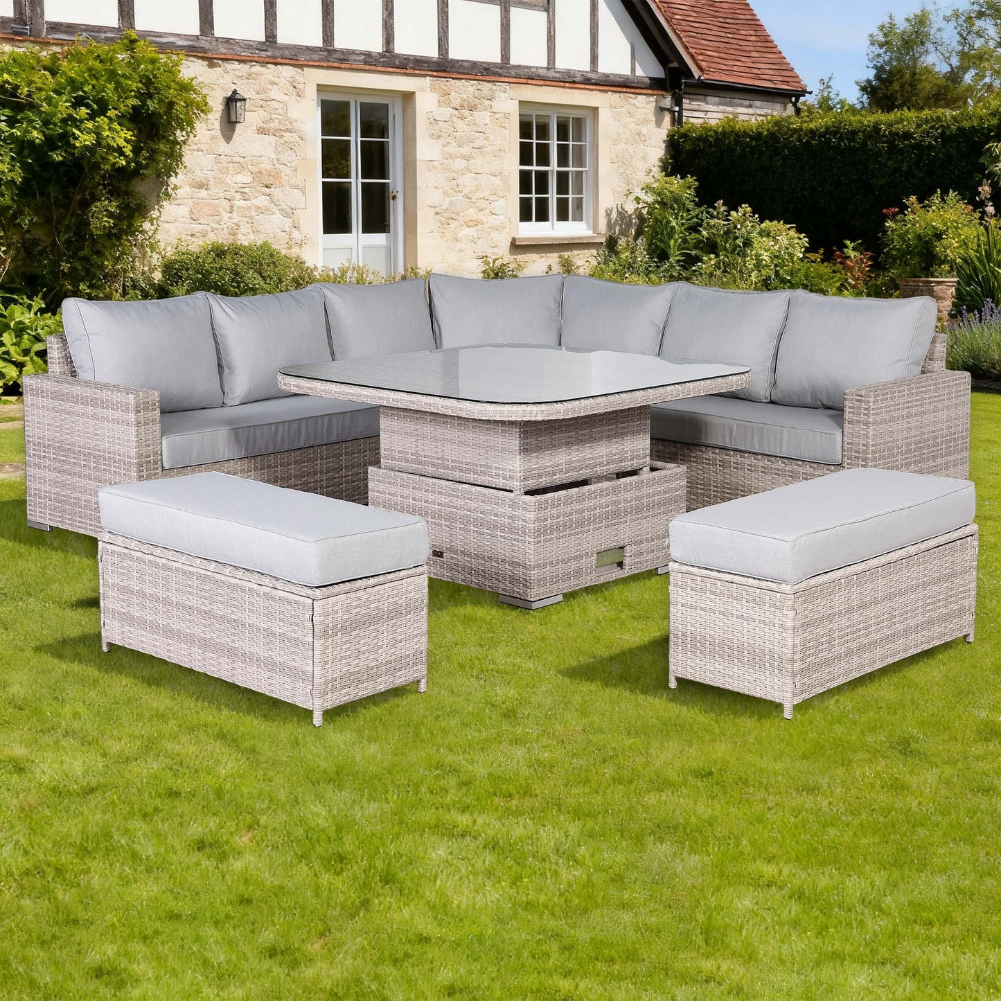 Garden furniture set with sofa, table, and ottomans on grass in front of a house.