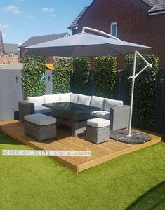 Monte Carlo Rattan Wide Corner Sofa Dining Set In Grey. Situated in the corner of a garden with a matching umbrella, on pine decking with Green grass.